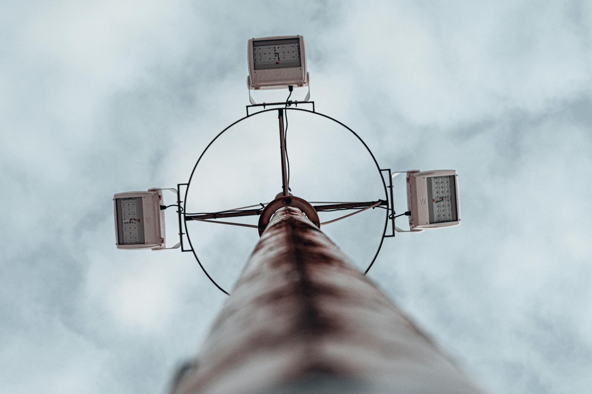 Dramatic low angle shot of a high mast lighting pole against an overcast sky.
