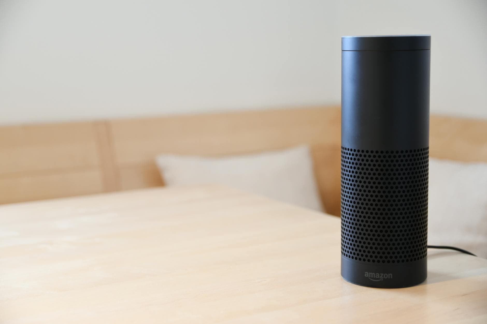 A black smart speaker resting on a light-colored wooden table in a cozy indoor setting.